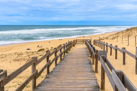 Wooden boardwalk path leading down to the sandy messanges beach, with people enjoying the ocean