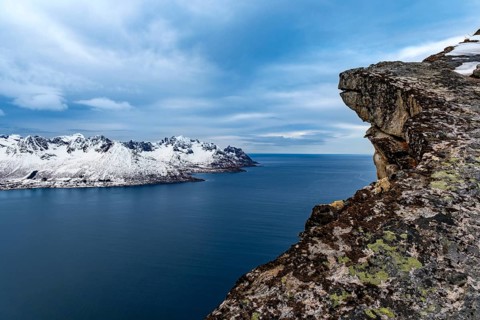 View over rocks to Mefjorden fjord and snowy mountains behind it, Senja island, Troms, Norway