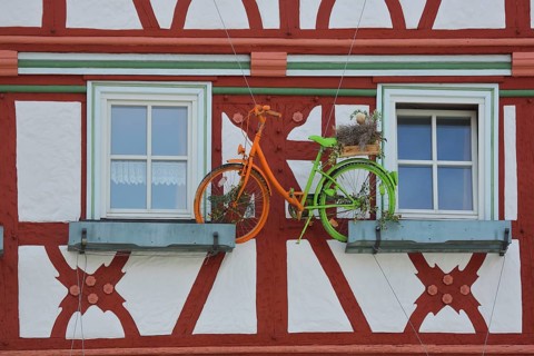 Brown-red house facade with floral decoration and colorful bicycle, two windows, half-timbered