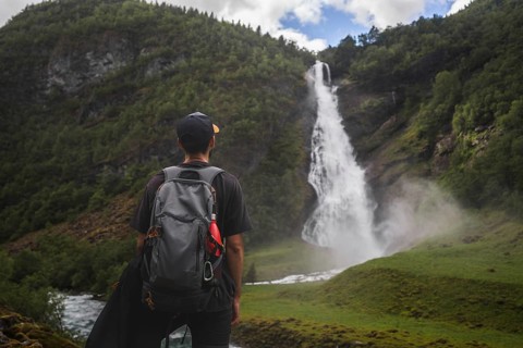 A captivating scene of a traveler with a backpack looking at a cascading waterfall amidst lush