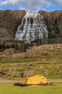 Tent, camping, man lying on the ground and sleeping, mountain bike, waterfall behind, sunny, cloudy