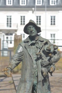 Sculpture De Saublacke by Kurt Grabert 1990, pig herdsman carries piglet in his arms, pig figure,