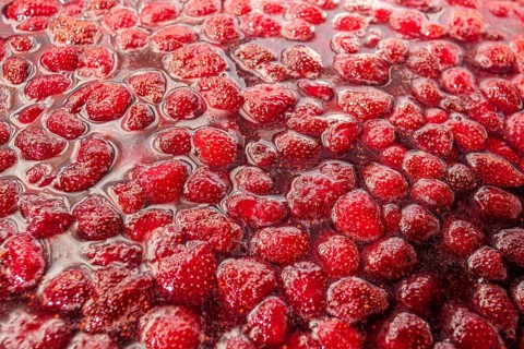 A close up shot of homemade strawberry jam, showcasing its vibrant red color and glistening texture