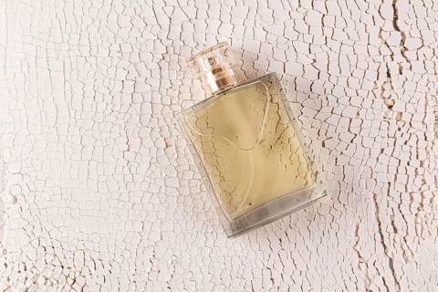 A transparent male perfume bottle rests on an aged, sand white surface The textured background