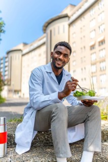 Vertical photo of a young african doctor eating healthy salad on a break outside the hospital