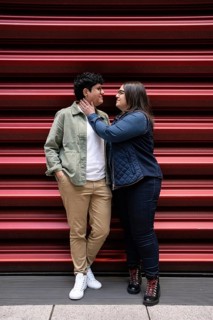 A loving curvy lesbian couple stands close, sharing an intimate moment against a vibrant red
