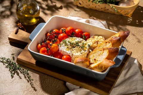 A deliciously baked Camembert cheese with cherry tomatoes, garlic, and toasted bread slices,