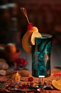 Cocktail in a glass with ice cube cubes, decorated with lime slices and cherries on a sandy
