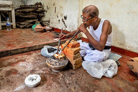 Man blows a flame with a pipe using a traditional workshop technique, a man burns sapphires in a