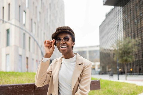 A black woman exuding confidence and style, wearing sunglasses and a hat in a modern urban setting