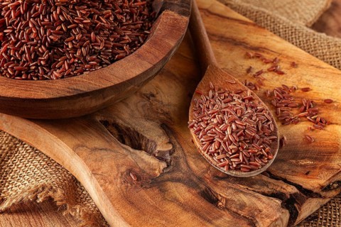Natural, red rice, in a wooden bowl and spoon on a wooden surface in rustic style, top view