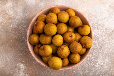 Ripe Longan in ceramic bowl on brown concrete background, top view, flat lay, close up, minimalism