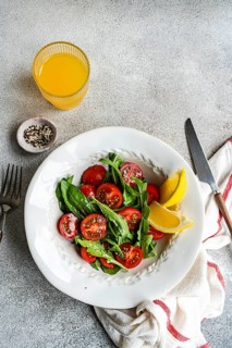 A fresh arugula and herb salad featuring cherry tomatoes, seeds, and Himalayan salt, drizzled with