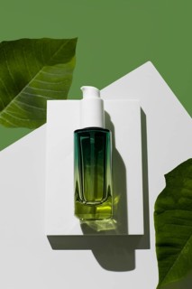 A green glass bottle of essential oil rests on a modern white stand against a striking green