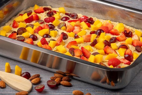 Unbaked fruit cake in the shape of topped with mango, strawberries and grapes