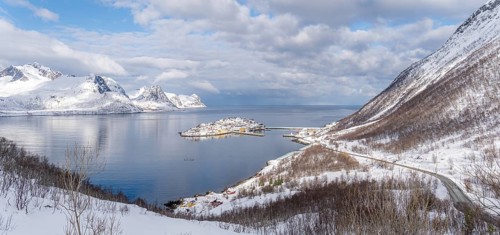A stunning winter landscape of Husoy, Norway, featuring snow-capped mountains, a serene island