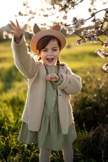 A joyful little girl in a hat is waving and smiling by almond blossoms during a beautiful spring