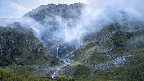 Mountain landscape with waterfalls and clouds on Lake Marian. Fiordland National Park, Southland