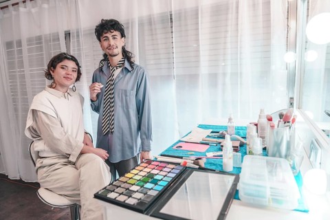 Two makeup artists are getting ready for a photoshoot, surrounded by their tools and equipment in a