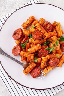 Rigatoni pasta with spicy sausage, and rich tomato sauce served, on a white plate, homemade
