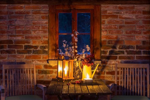 Still life with candles on a table, chairs next to it, it's getting dark outside, cozy atmosphere