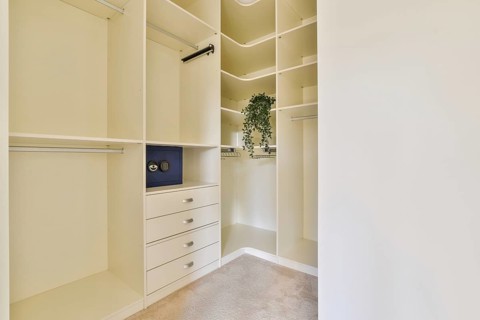 A spacious and modern walk in closet featuring built in shelves and drawers in a bright, neutral