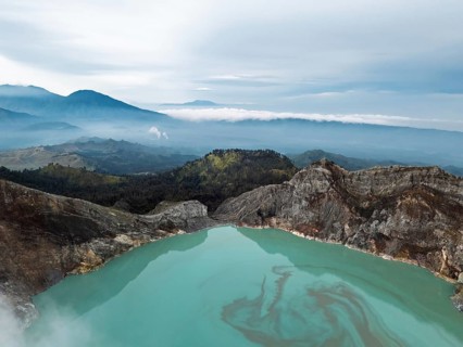 Expansive view of the turquoise lake at Ijen crater surrounded by forested hills and volcanic