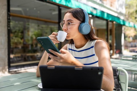 A young woman enjoys a day in the city, sipping coffee while connected to technology. She wears