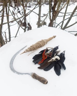 Spindle, crow feathers, bird skull and rowan beads and sickle in the snow. Still life. Pagan,