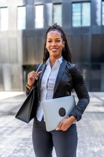 Vertical portrait of a latin businesswoman carrying laptop and bag standing in the city