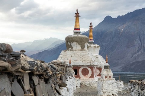 Ancient stupas stand against the backdrop of majestic mountains and a dramatic sky in Diskit, Nubra