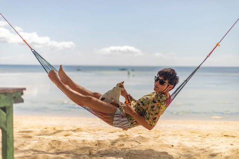 A woman lounges in a colorful hammock on a sandy beach in the Philippines, sharing a playful moment