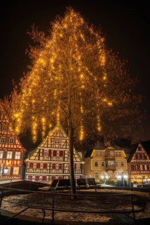 A festively lit tree in front of illuminated half-timbered houses on a winter's night, Calw
