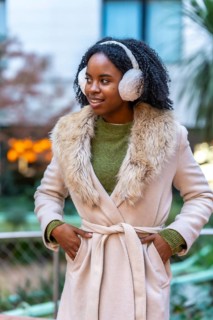 Smiling young woman wearing winter clothes and earmuffs enjoying a winter day in the city