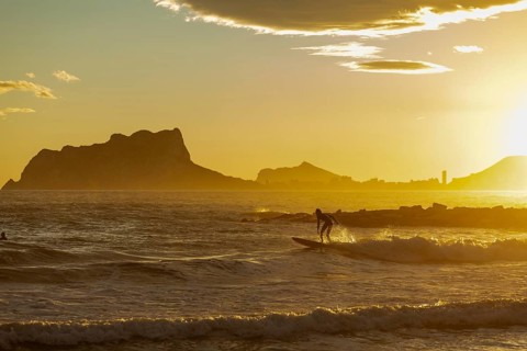 A surfer is silhouetted against the backdrop of a stunning sunset over the Mediterranean Sea off