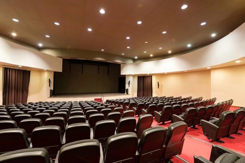 An empty convention center features rows of comfortable seats, bright stage lights, and elegant
