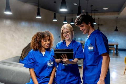 Three smiling healthcare students in blue scrubs working together and sharing information on a