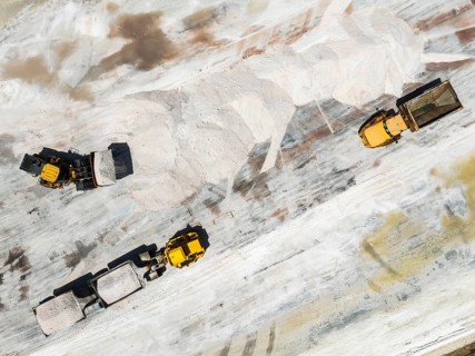 Excavator and lorries and at a harvesting pan of the Walvis Bay Salt works. Aerial view. Drone shot
