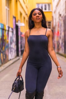 Fashionable urban style with a black African girl in a black suit and high boots on a city street.