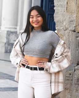 A young woman poses confidently in a chic urban setting, wearing a trendy plaid jacket over a gray