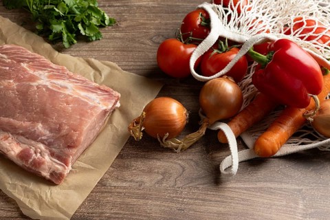 Fresh ingredients for Hungarian pork goulash, including pork, tomatoes, onions, carrots, and bell