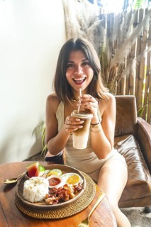 Happy tourist sipping iced coffee while enjoying a traditional filipino breakfast of bacon, eggs,