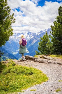 Person with rucksack enjoying the view of snow-covered mountains from a hiking trail, Penken,