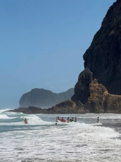 Surfer at Piha Beach with open surf and rock Lion Rock near Auckland, North Island, New Zealand,