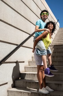 A joyful multiethnic LGBTQ+ couple shares a lighthearted moment on outdoor stairs. One carries the
