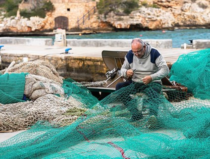 A fisherman ties and repairs his net in the port of Cala Figuera, Majorca, Spain