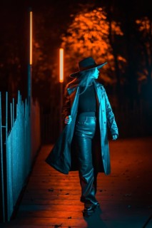 Caucasian brunette girl with hat at night in a park illuminated with blue light. Winter fashion and
