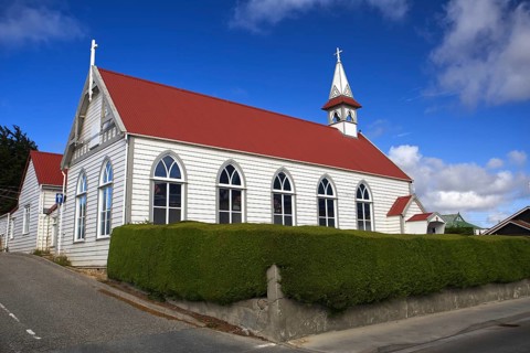 White wooden church with red roof and blue sky in the background, surrounded by manicured hedges,