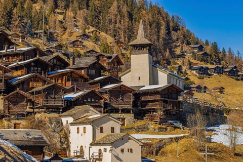 Snow-covered roofs of old farmhouses and barn storage, white cellars, Saint Theodule church in the