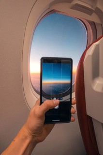 Cropped unrecognizable person captures a sunset over the ocean using a smartphone, viewed through